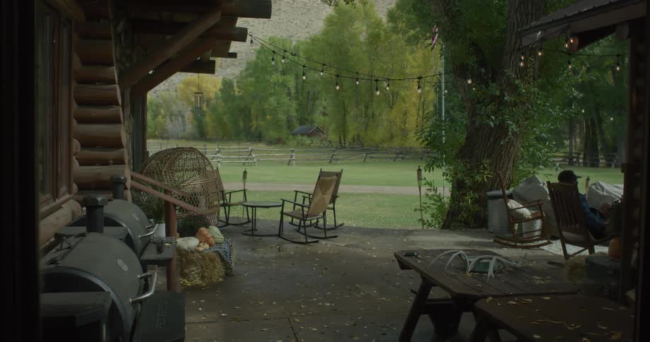 Rustic patio with rocking chairs overlooks a grassy field and autumn trees