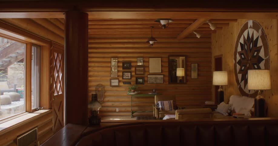 Cozy room with woodpaneled walls green console under framed art cushioned chair and a sculptural treebranch wall piece as a man steps out the door