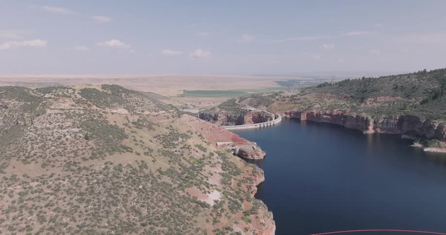 Aerial view of a large dam nestled between rocky hills and a calm blue reservoir