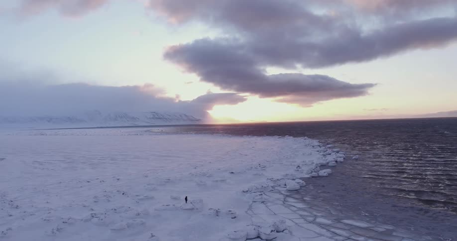 A large snow covered area with some water and a man walking across it