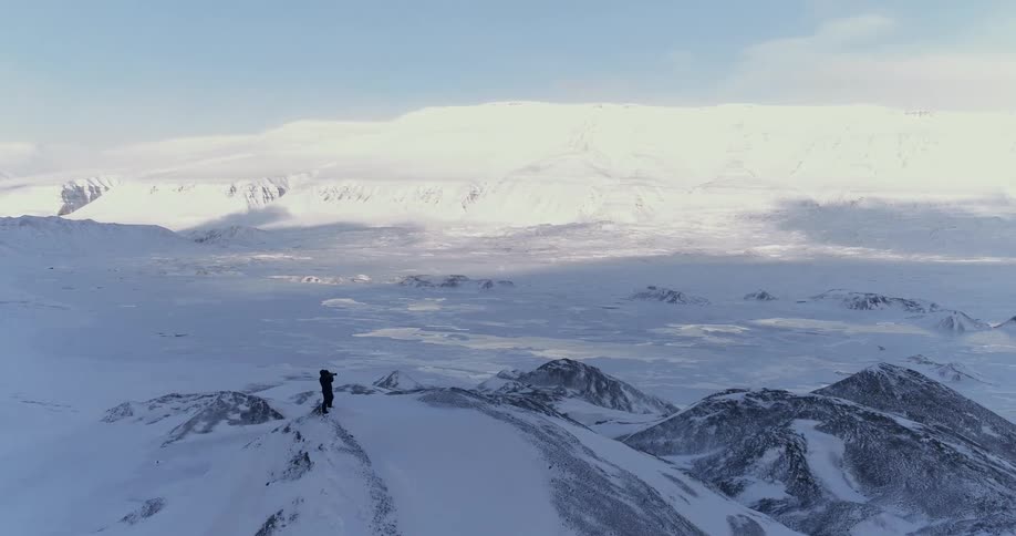 A man standing on a large hill in an open field that is covered with snow