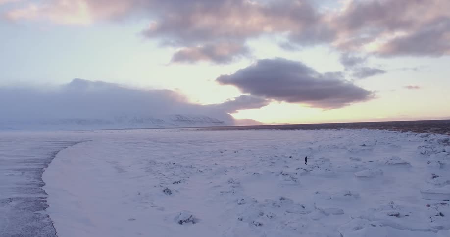 A man is hiking along a vast snow covered shore