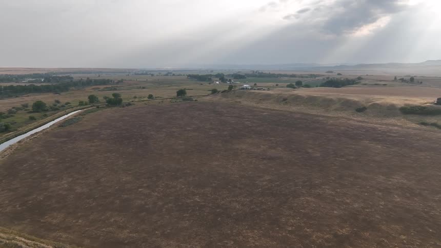 River runs around an empty field near a lonely house