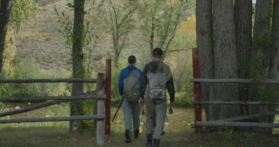 Three men with fishing equipment walking towards the river