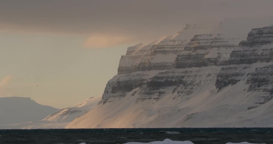 Dark clouds hang over the sea and a frozen landscape at dusk