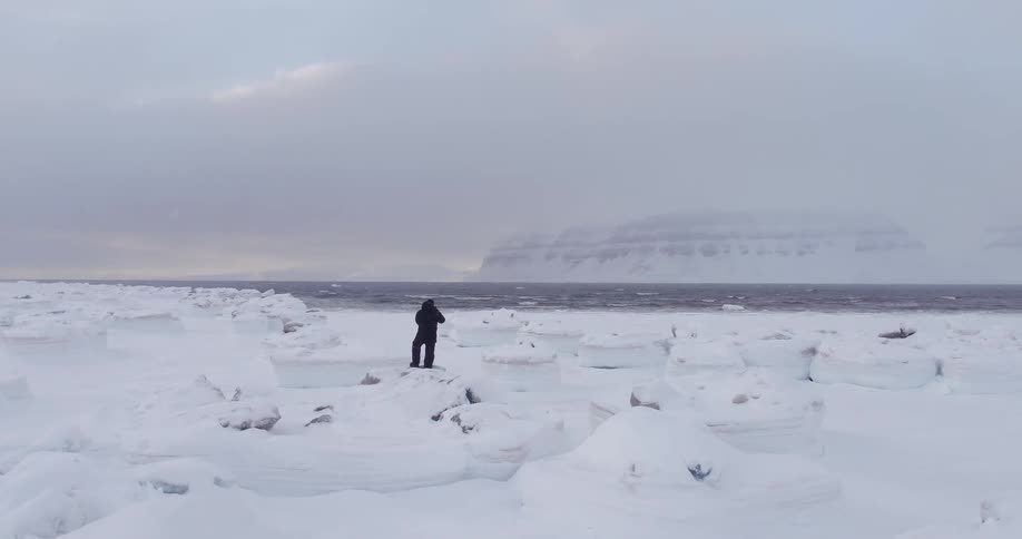 A man is standing on some rocks by an icy shore