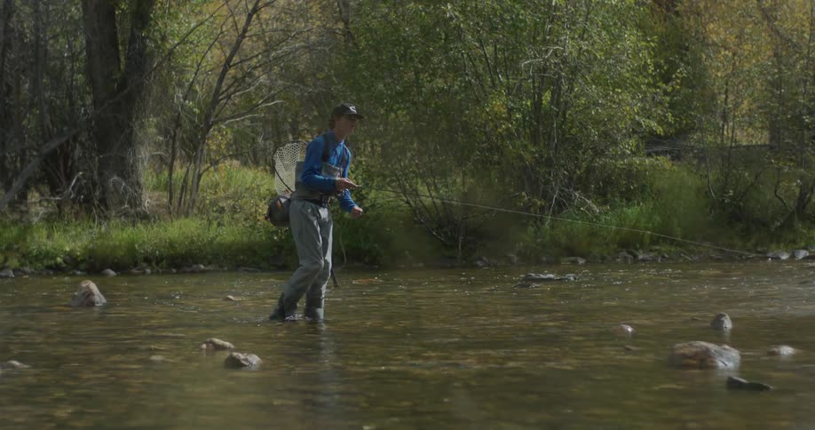 A man is fly fishing in the river and carrying a pole and net
