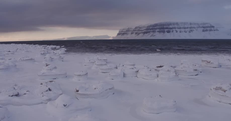 Dark clouds hang over the sea and a frozen landscape