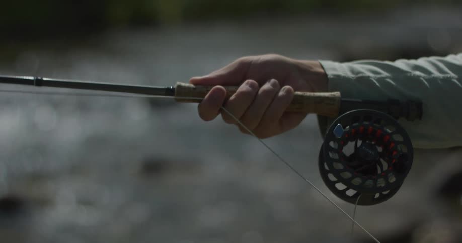 Closeup of hands holding a fishing rod over a blurred river background