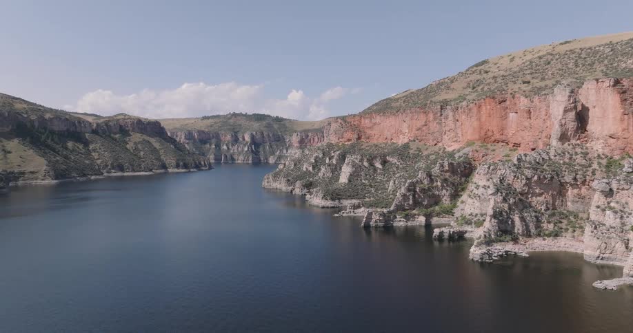 An aerial shot captures a wide calm river flowing through a dramatic canyon with steep rocky cliffs under a bright blue sky