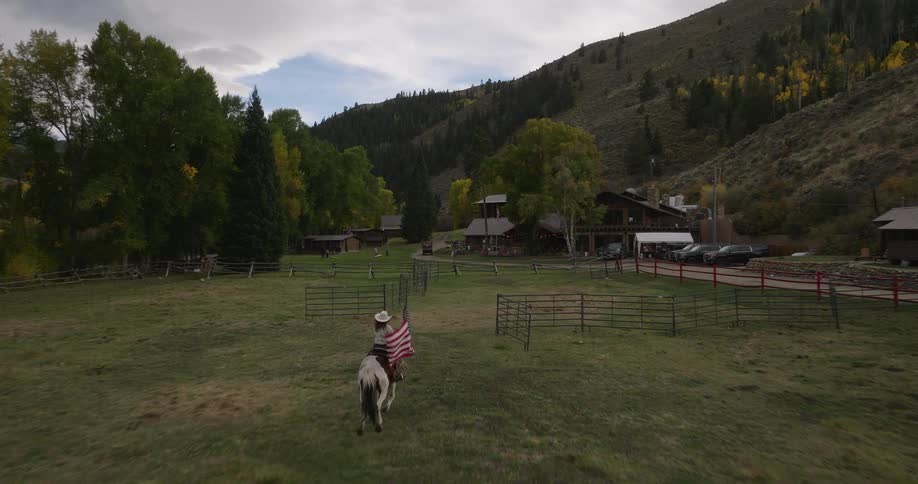 A woman carrying an american flag rides her horse into the ranch