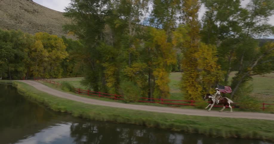 Woman running with a horse at high speed along a lake and carrying an american flag