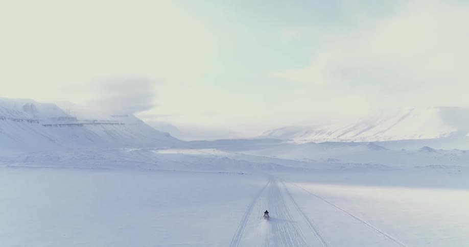 A snowmobile drives across a snow-covered landscape during daylight