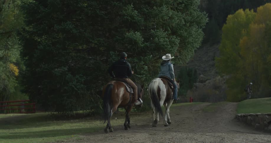 Man and woman riding horses along a trail with mountains in the background