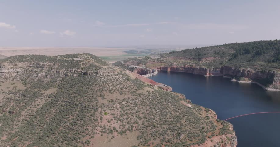 A wide aerial view of a large canyon lake surrounded by hills and a distant dam structure