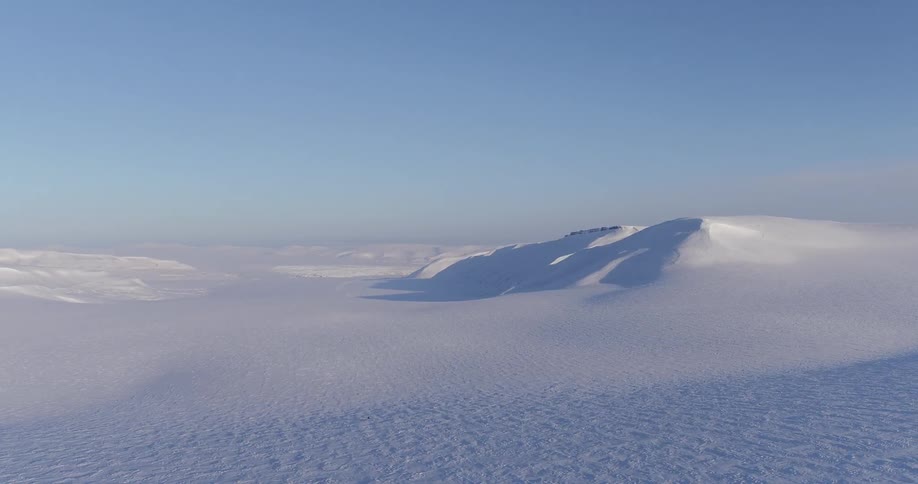 The long snow covered field leads to mountains on a sunny day