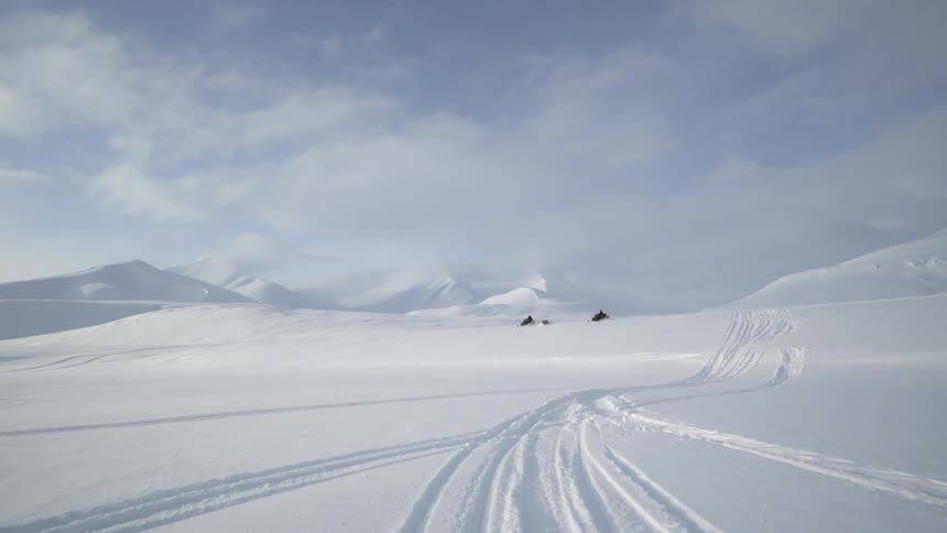 Snow mobiles race down a snow covered field on a cloudy day