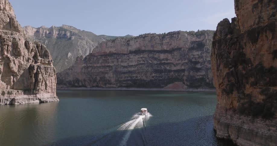 A small boat moves through a calm canyon lake surrounded by steep rocky cliffs