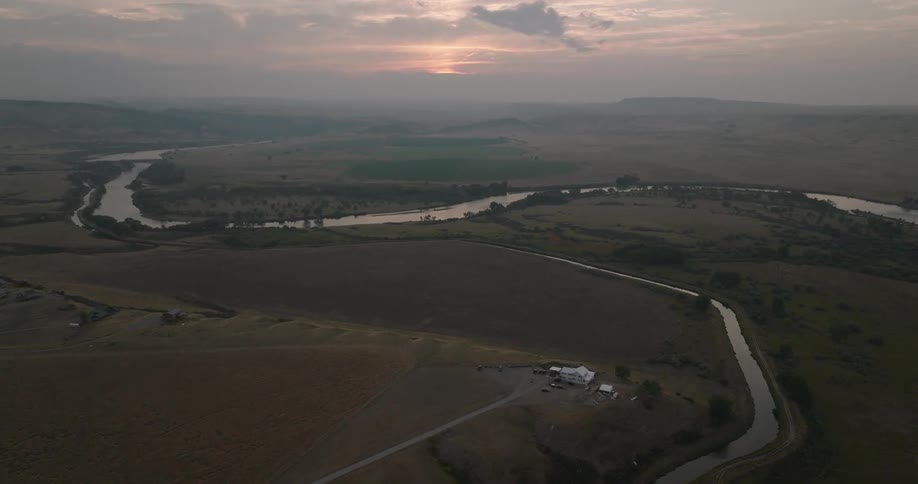Aerial view of a winding river cutting through vast rural land at sunset