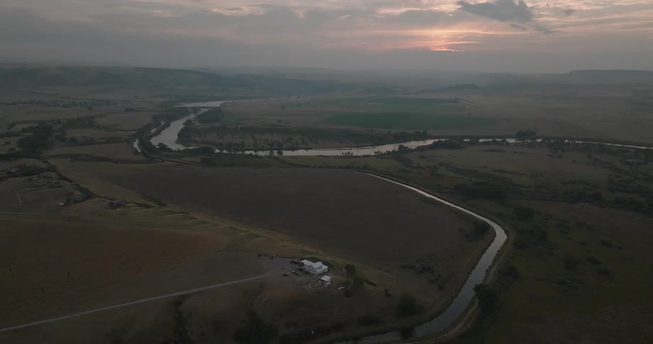 The image shows an aerial view of a winding river cutting through wide open plains at sunset