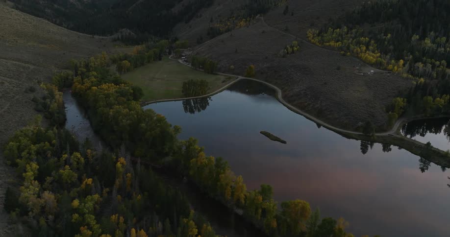 Aerial view of a calm lake surrounded by autumn trees and rolling hills during dusk