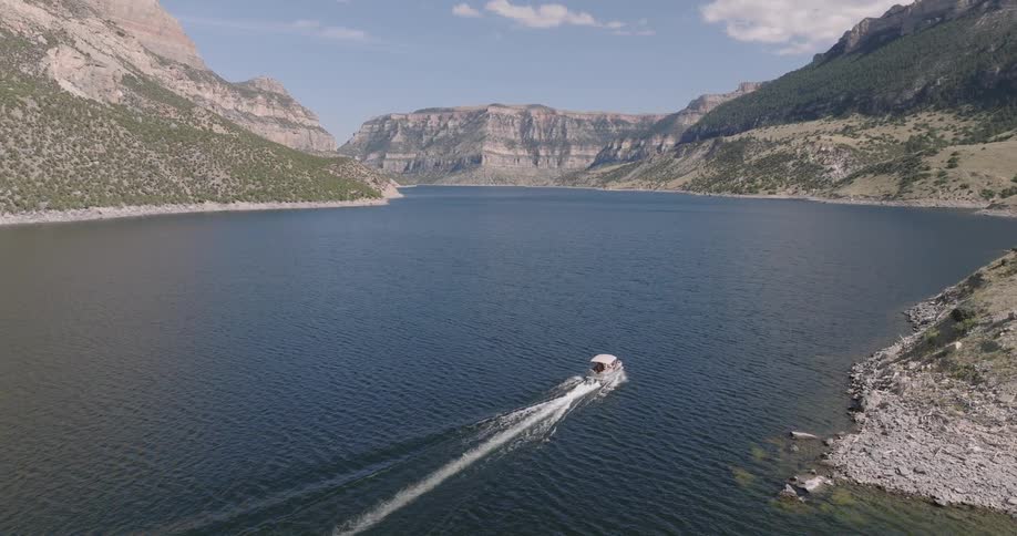 A small boat moves across a wide mountain lake under clear skies