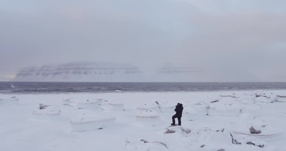 A man is taking photographs near a snowy shore
