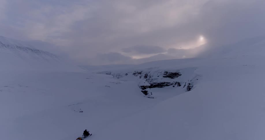 Person riding snowmobile through snow covered arctic wilderness