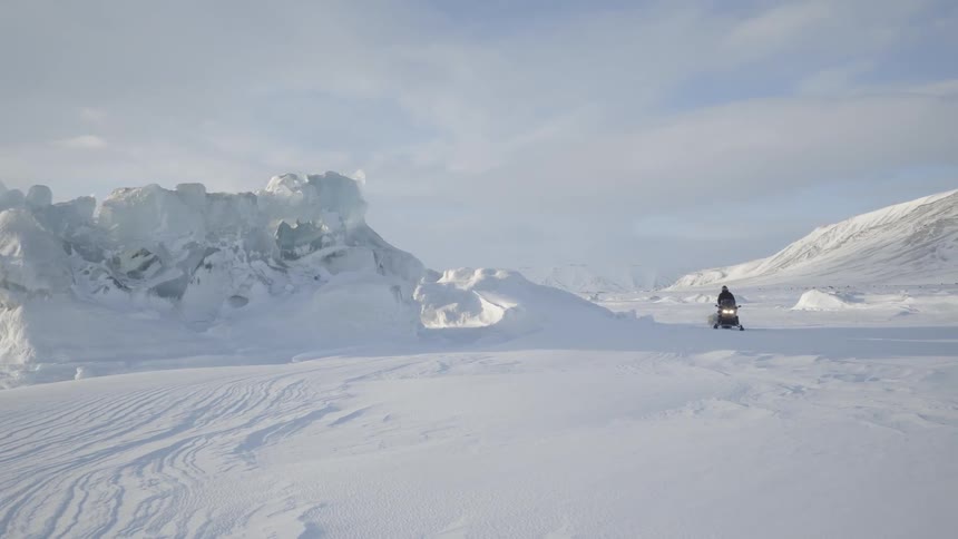 A snowmobile drives across a snow-covered landscape during daylight