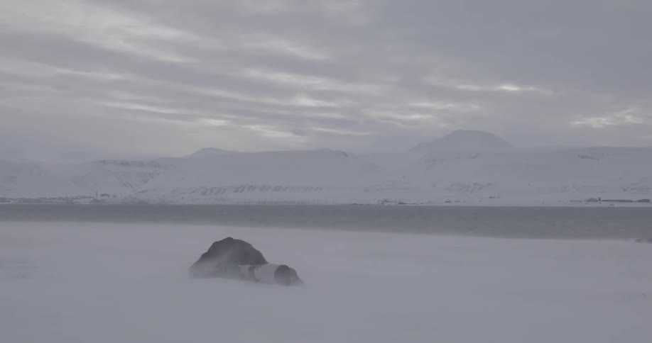 A photographer lays in the snow as snow is blown around him