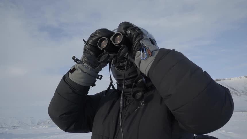 A person is using binoculars on a snow covered field