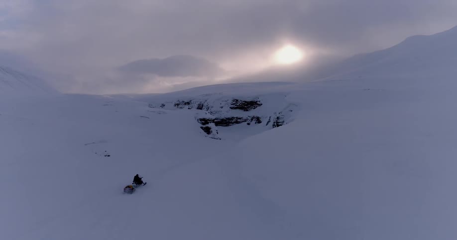 A snowmobile races along the snow covered mountain