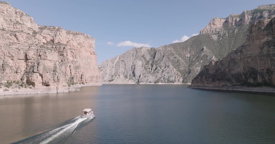 A powerboat creates a wake as it travels through a wide canyon with towering rock formations on either side