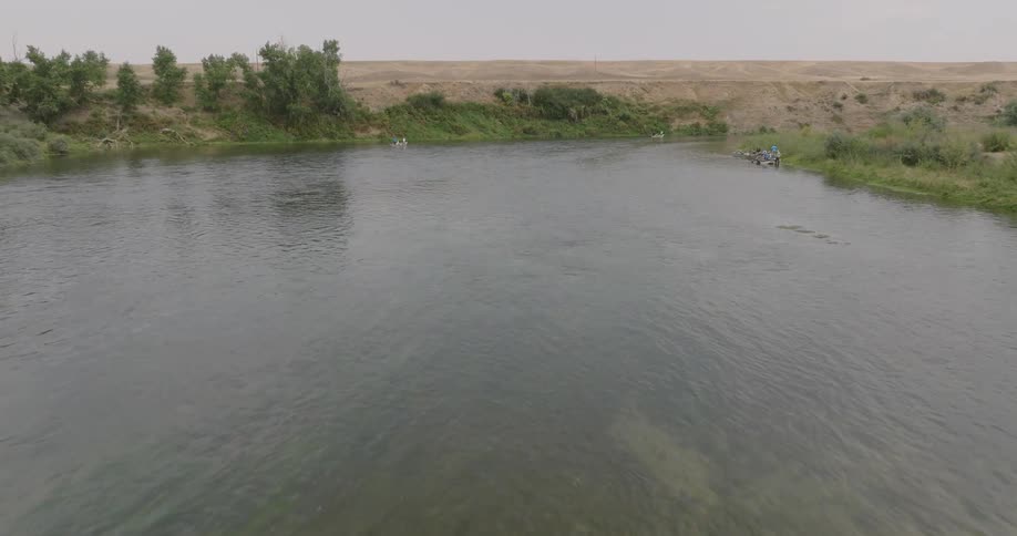 Aerial view of a river surrounded by vegetation and people in small boats on the shore