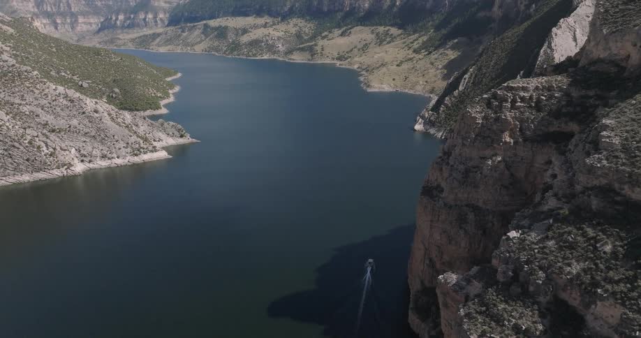 A boat moves through a calm canyon river captured in a wide aerial shot