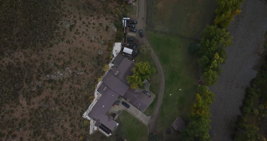 Rural house seen top down surrounded by trees grass and vehicles