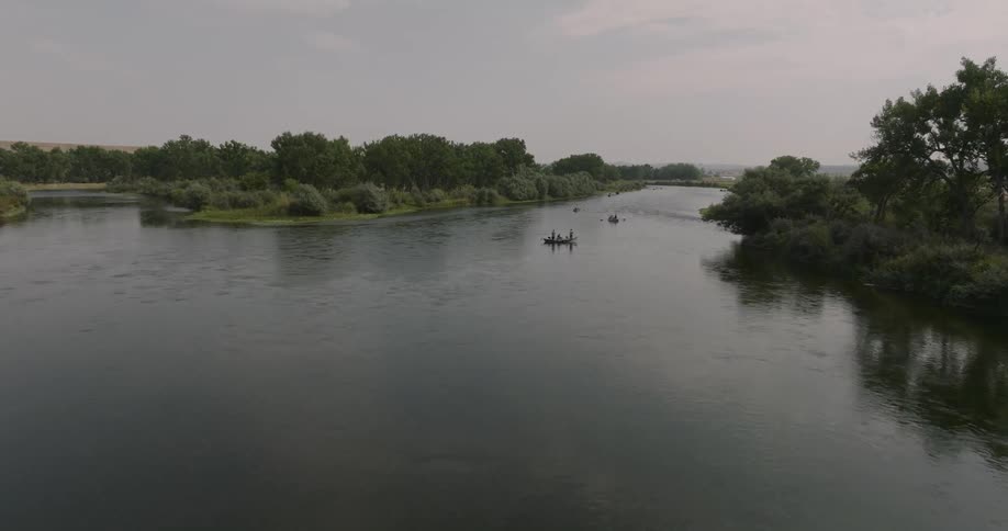 People occupy boats floating in one side of a river fork on an overcast day