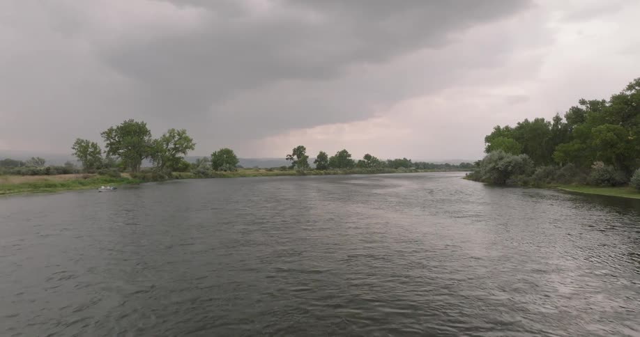 A wide view of a river under a storm sky with dark low clouds gathering over calm water