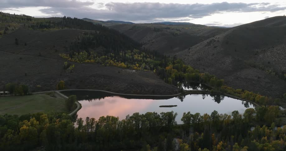 Aerial view of a lake surrounded by trees and hills under a cloudy sky