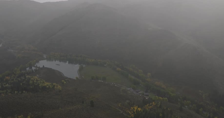 An aerial view shows a lake and river in a valley surrounded by hazy mountains
