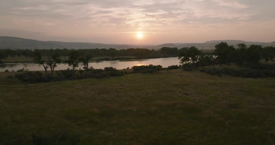 A wide aerial shot shows a grassy field and river at sunrise