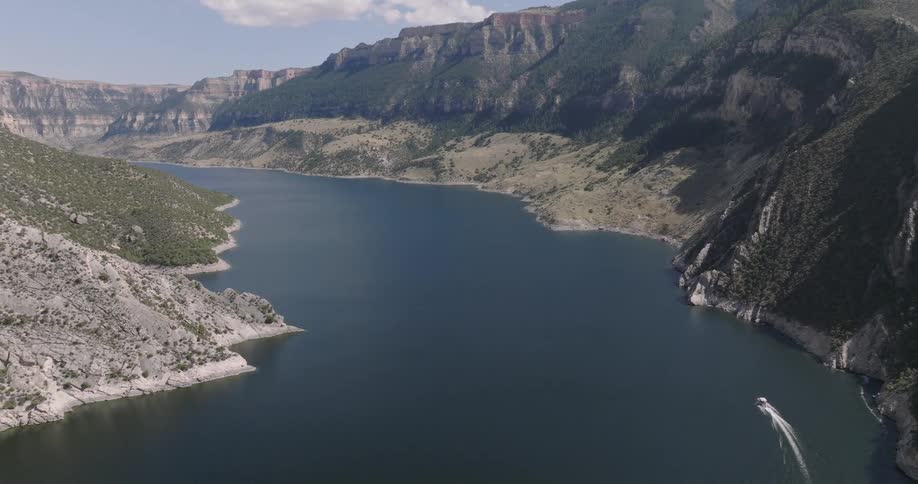 A lake with mountains lining the right side as a boat moves across the water at midday