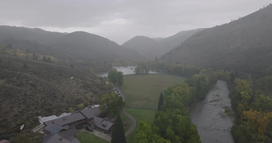 A misty aerial view of a riverside house in a forested mountain valley