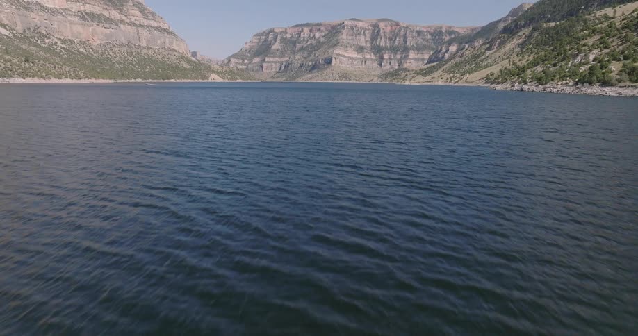 A wide lake stretches beneath rugged mountain cliffs under a clear blue sky