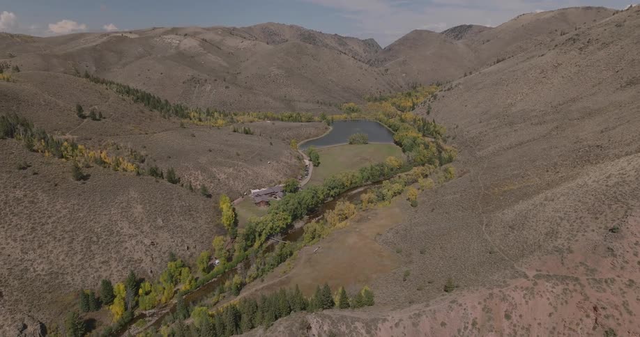 A winding river and small lake sit nestled in a valley surrounded by dry hills and scattered trees