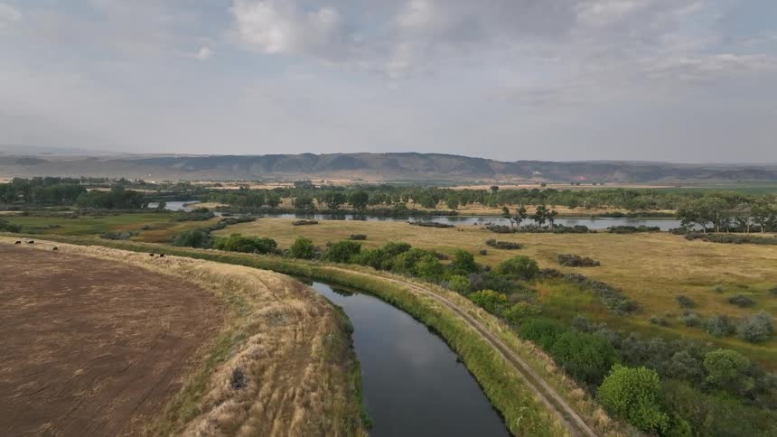 A narrow river flows through farmland and grassy plains