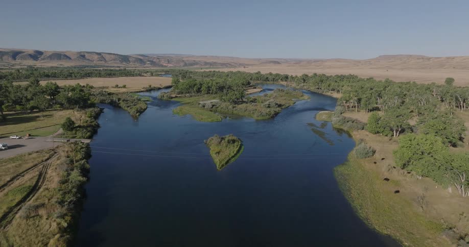 A river curves through grassy plains with trees and parked rvs nearby
