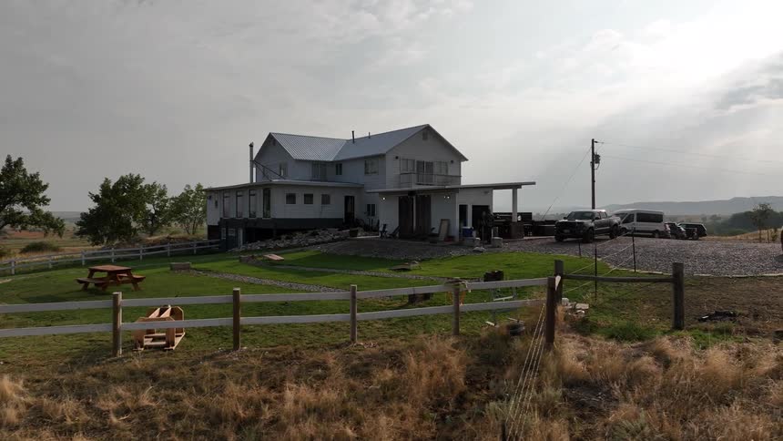 A modern house with parked vehicles sits in a dry rural area