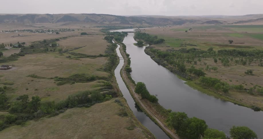 Aerial view of a vast river with towering mountains on the horizon on a cloudy day