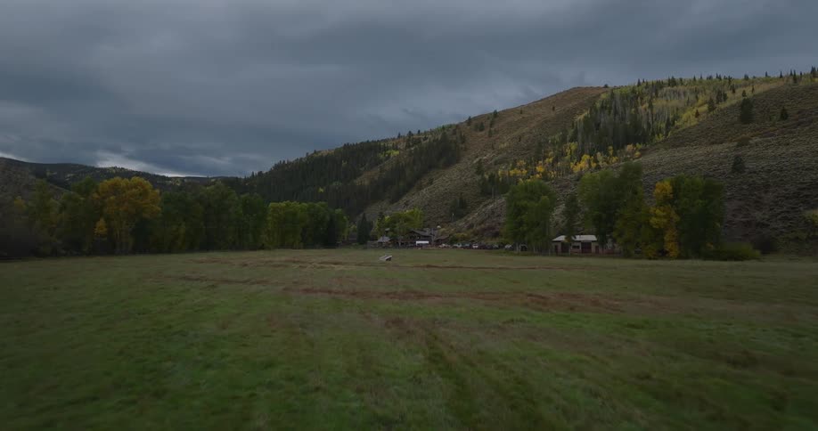 A farmland enclosed by a wooden fence with lush grassland stretching across the field and mountains encircling the landscape in the background